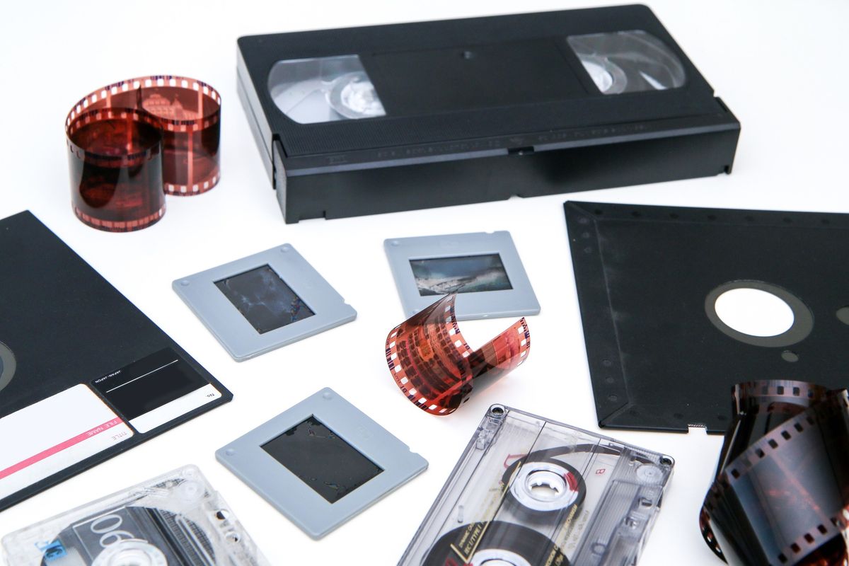 VHS tapes, film reels, photo slides, audio cassettes, and negative strips on a white table
